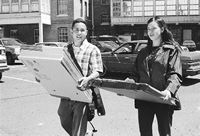 Ian Nicolas and Abbey carrying folded boxes, walking in the parking lot 