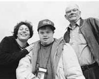Maria Buezo smiling with her hand on Gerry, who is wearing a cap, his father in the background.