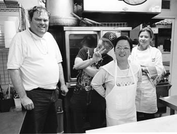 Clients standing in a industrial kitchend wearing aprons, wtih Chef Allison Owns in the background
