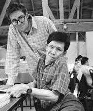 John standing behind a woman woring at a table. The worman appears to have motor difficulties