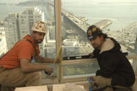 Two glaziers by a window overlooking the bay bridge