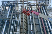 worker in a lift next to a wall of heating pipes